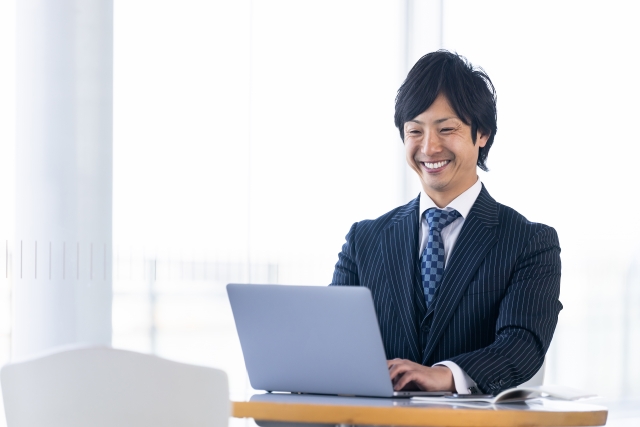 スーツをきた男性がパソコンで笑顔で仕事をしている